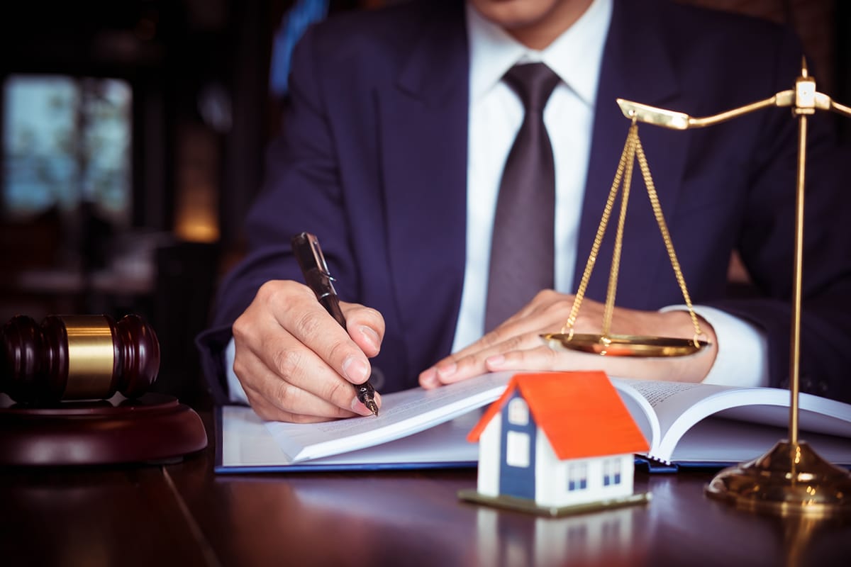 Real estate legal professional finalizing documents, a scale of justice and gavel in view, with a house model, reflecting recent NAR settlement changes.