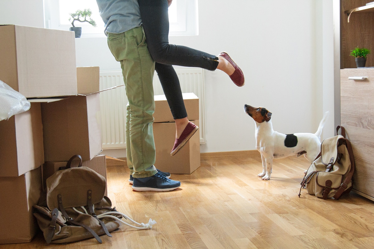 Excited new homeowners with a dog amidst moving boxes, celebrating their first home purchase in Arizona.