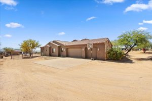 Side view of 3-car garage and driveway at 28025 N 156th Place, Scottsdale, showing desert landscaping and gated access to horse facilities