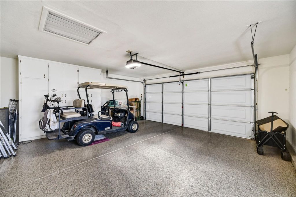Oversized garage with epoxy flooring, built-in storage cabinets, and optional golf cart at 18410 N 104th Avenue, Sun City