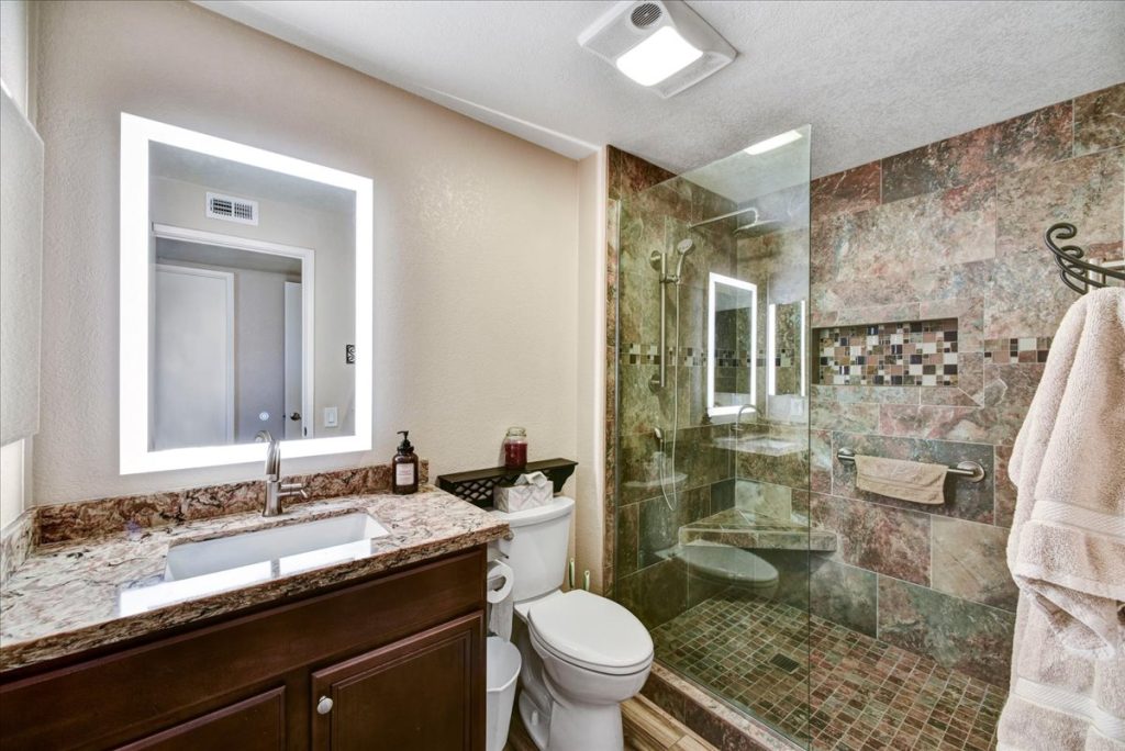 Remodeled master bathroom with quartz countertop, walk-in shower, and backlit vanity mirror at 18410 N 104th Avenue, Sun City