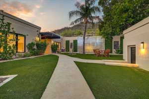 Front courtyard at 6432 E El Sendero Rd in Carefree, AZ, featuring a modern water wall, palm tree, and outdoor seating area surrounded by artificial turf and greenery.